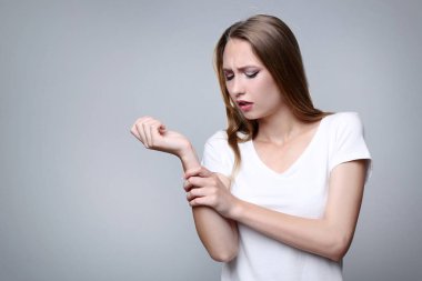 Gri arka plan üzerinde Bilek ağrısı olan genç kadın