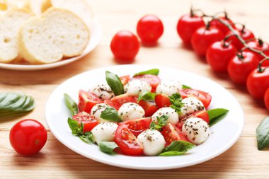 Mozzarella peyniri, domates ve fesleğen yaprakları üzerinde kahverengi ahşap masa