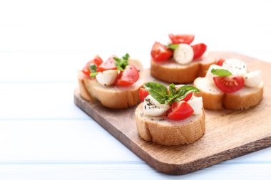Ahşap kesme tahtası üzerinde Bruschetta mozzarella peyniri, domates ve fesleğen yaprakları