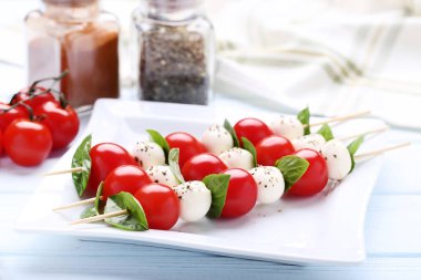 Ahşap masa üzerinde mozzarella peyniri, domates ve fesleğen yaprakları ile sopa