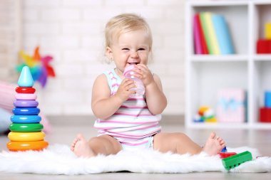 Beyaz halı üzerinde oturan şişe ile kız bebek