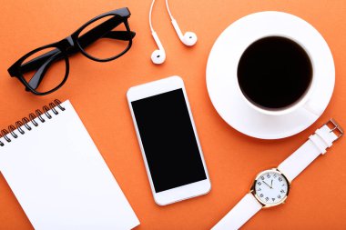 Smartphone ile kulaklık, fincan kahve, defter ve Bilek seyretmek turuncu zemin üzerine