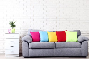 Beyaz başucundaki gri kanepe ve tuğla duvar arka plan üzerinde renkli yastıklar