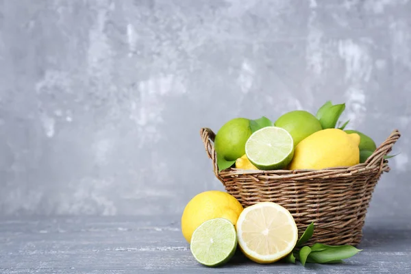 Lemons and limes with green leafs in basket on grey wooden table