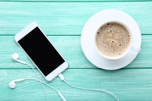 Smartphone with earphones and cup of coffee on wooden table