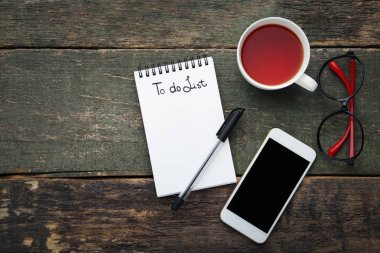 Fincan çay, gözlük ve gri ahşap masa üstünde smartphone ile not etmek içinde listelemek için