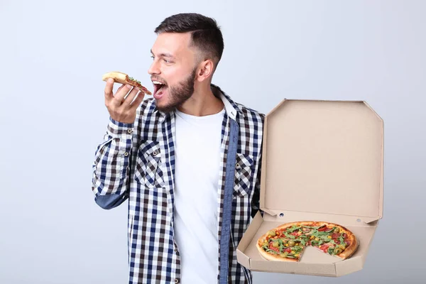 Ung Man Äter Pizza Och Hålla Kartong Grå Bakgrund — Stockfoto