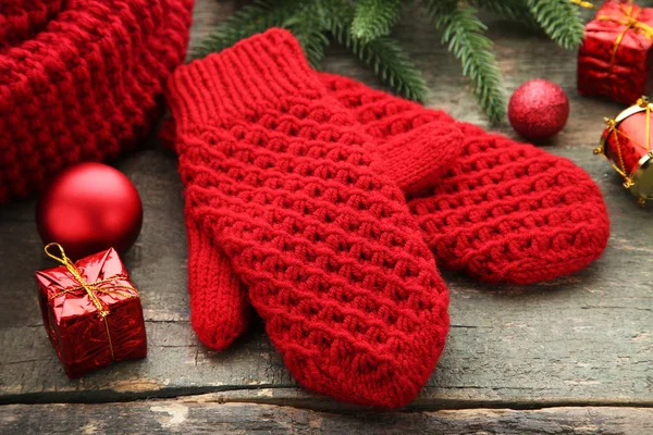 Knitted red gloves with christmas decorations on wooden table