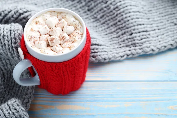 Cappuccino with marshmallows in cup and knitted scarf on wooden table