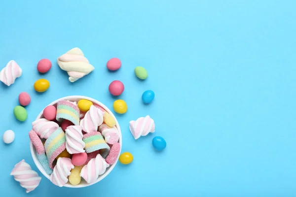 Sweet candies in bowl on blue background