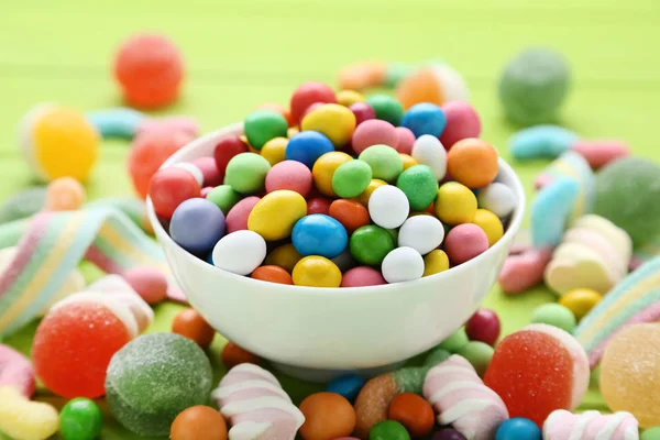 Colorful sweet candies in bowl on green background