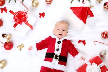 Kırmızı kostümlü Noel süslemeleri ile yatakta yatarken erkek bebek