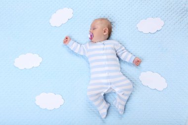 Mavi yatakta uyuyan kağıt bulutlar ile erkek bebek