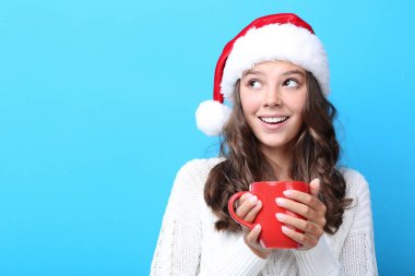 Noel Baba şapkası çay mavi arka plan üzerinde tutan güzel kız