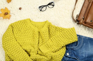 Kot pantolon, deri çanta ve akçaağaç ile örme kazak beyaz halı üzerinde yapraklar