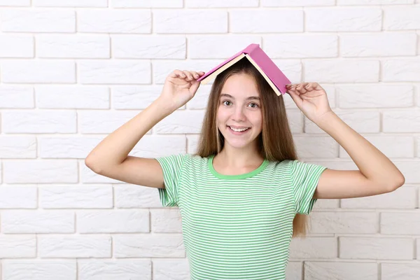 Menina Feliz Segurando Livro Sua Cabeça Fundo Parede Tijolo Branco — Fotografia de Stock