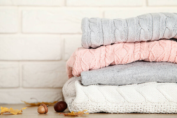 Stack of folded sweaters with acorn, chestnut and autumn leaves on brick wall background