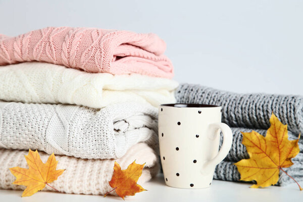 Stack of folded sweaters with cup and maple leaves on grey background