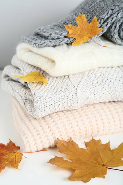 Stack of folded sweaters and scarf with autumn leaves on grey background