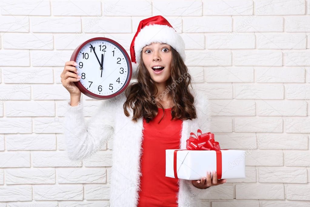 Beautiful girl holding round clock and gift box on brick wall background
