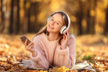 Genç güzel kız smartphone Sonbahar Park ve kulaklık ile yalan