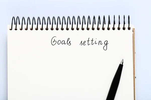 Goal setting in notepad with pen on grey background