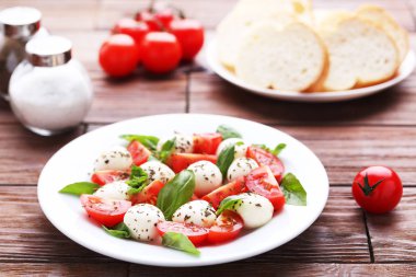 Mozzarella peyniri, domates ve fesleğen yaprakları üzerinde kahverengi ahşap masa