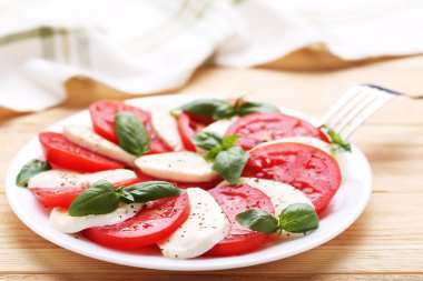 Mozzarella peyniri, domates ve fesleğen yaprakları üzerinde kahverengi ahşap masa