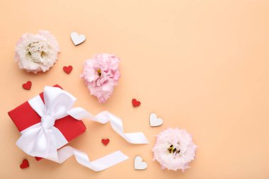 Bej renkli arka plan üzerinde şerit ve eustoma çiçekli hediye kutusu