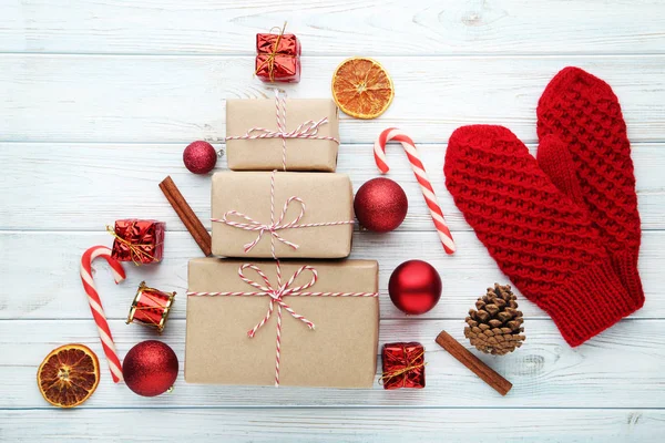 Knitted red gloves with gift boxes and christmas decorations on wooden table