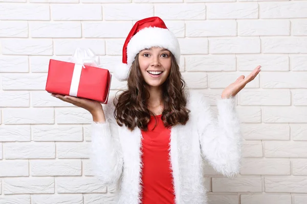 レンガ壁の背景にギフト ボックスを保持サンタ帽子で美しい少女 — ストック写真