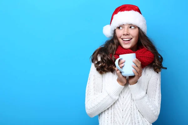 美丽的女孩在圣诞老人帽子和围巾拿着一杯茶在蓝色背景 — 图库照片