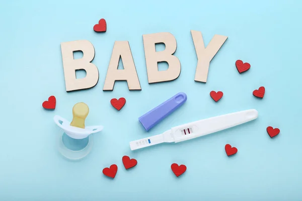 Pregnancy test with pacifier and red hearts on blue background