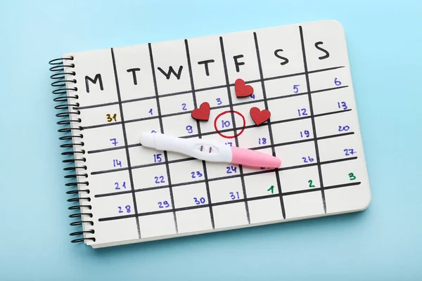 Hamilelik testi ile mavi arka plan üzerinde kağıt takvim ve kırmızı kalpler