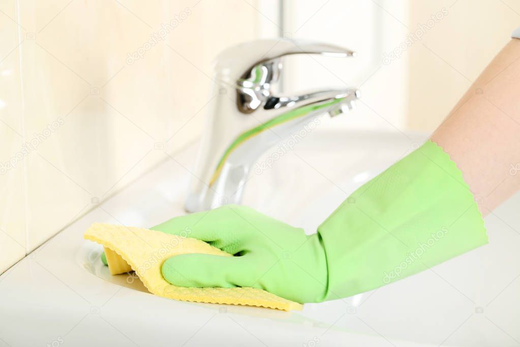 Hand in green glove cleaning water tap in bathroom