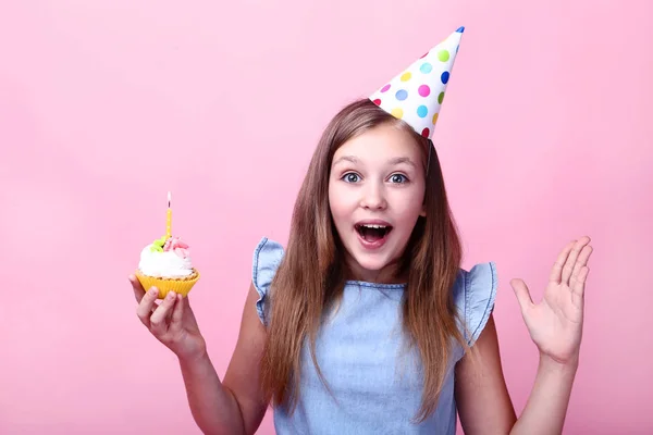 ピンクの背景にカップケーキを持って誕生日帽子の感情的な少女 — ストック写真
