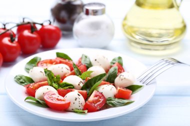 Mozzarella peyniri, domates ve fesleğen yaprakları üzerinde ahşap masa