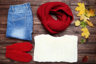 Kazak örme, eşarp. eldiven, kot pantolon ve akçaağaç yaprakları üzerinde kahverengi ahşap masa