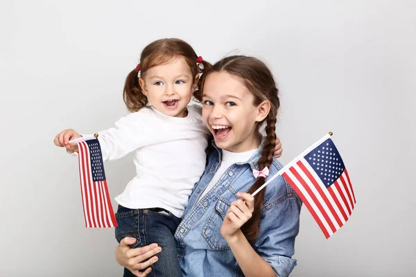 灰色の背景にアメリカ国旗を持つ二人の姉妹 — ストック写真
