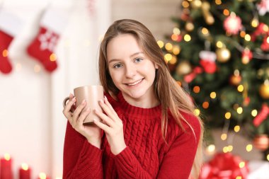 Evde yılbaşı ağacının yanında oturan Kupası ile genç kız