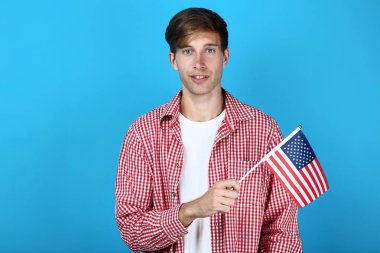 Genç adam bir Amerikan bayrağı mavi arka plan üzerinde tutan