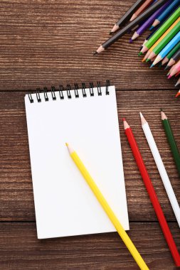 Kahverengi ahşap masa üzerinde defter olan renkli kalemler.