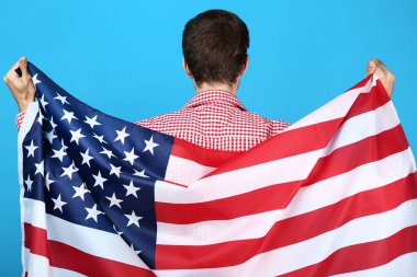 Genç adam bir Amerikan bayrağı mavi arka plan üzerinde tutan