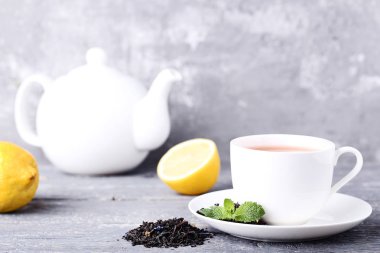 Nane ile çay yaprakları, limon ve eski püskü gri arka plan üzerine çaydanlık