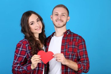 Mavi arka plan üzerinde kırmızı kağıt kalp tutan güzel genç çift