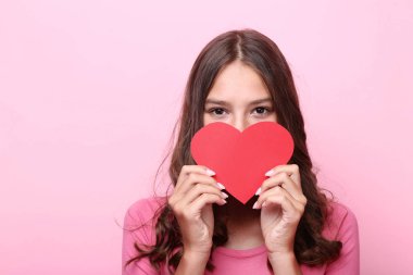 Pembe arka plan üzerinde kırmızı kağıt kalp tutan genç kız