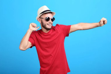 Güneş gözlüğü ve şapka mavi arka plan ile genç adam