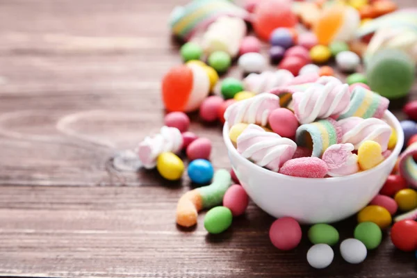 Colorful sweet candies in bowl on brown wooden table