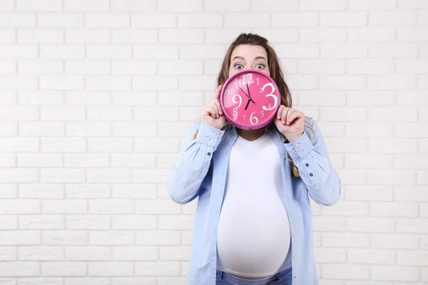 Hermosa Mujer Embarazada Sosteniendo Reloj Rosa Sobre Fondo Pared Ladrillo —  Fotos de Stock