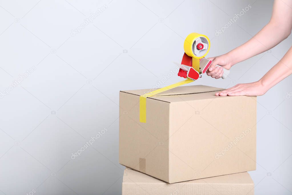 Female hands packaging cardboard box with dispenser on grey background